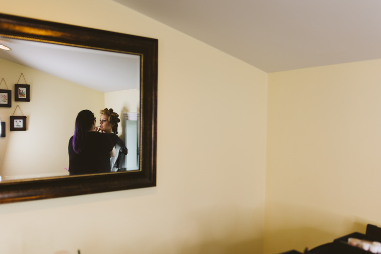 bride in mirror getting makeup put on