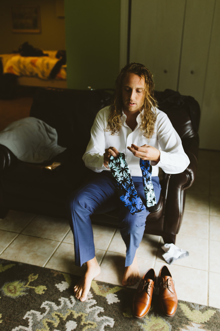 Casey the groom looking at his fun socks for the wedding blue ombre palm tree socks